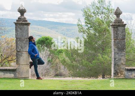 Middle-aged man leaning on a stone column while pensively looking at the sky Stock Photo
