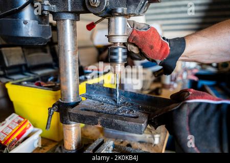 Crop man in cap and plaid shirt working with wooden detail on drilling machine in light garage Stock Photo