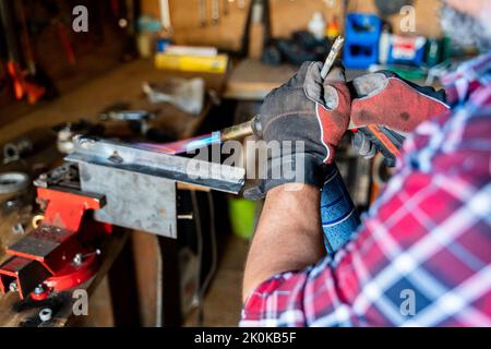 Crop carpenter in cap and gloves heating metal part with gas torch working in garage Stock Photo