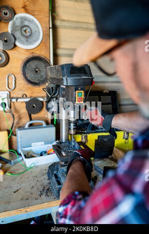 Crop man in cap and plaid shirt working with wooden detail on drilling machine in light garage Stock Photo