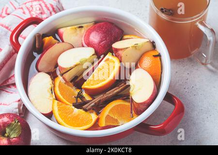 Cooking homemade hot cider from apples and oranges with spices in a red saucepan. Autumn or winter warming drink. Stock Photo