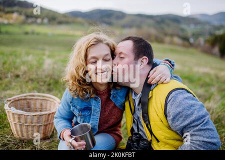 Outdoor portrait of man with down syndrome hugging and kissing his mother, during resting in green meadow. Stock Photo