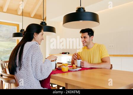 Attractive Hispanic happy lady and young guy having breakfast together at table in modern kitchen Stock Photo