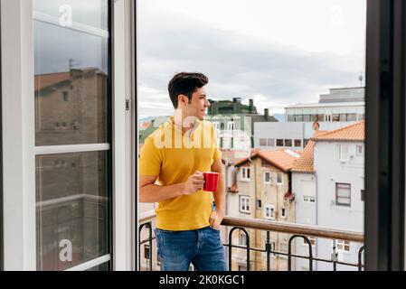 Attractive caucasian man with a coffee cup on the balcony at home looking away Stock Photo