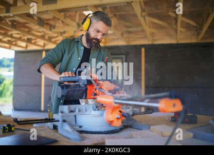 Construction worker working with eletric saw inside wooden construction of house, diy eco-friendly homes concept. Stock Photo