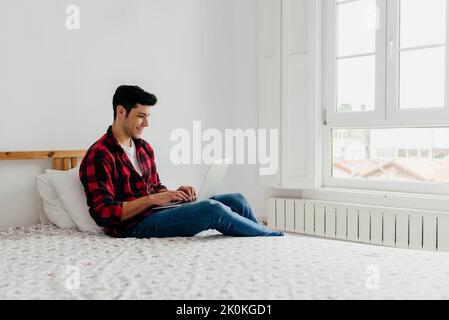 Side view of handsome caucasian man working on the laptop in bedroom at home Stock Photo