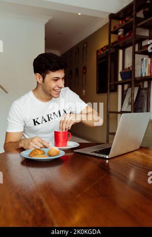 Handsome caucasian man having breakfast at home with laptop on the table Stock Photo