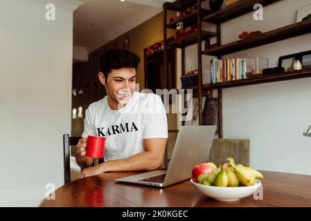 Handsome caucasian focused man drinking coffee at home while working on his laptop on the table Stock Photo