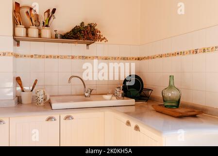 Ceramic kitchenware with utensils arranged on shelf and counter of stylish light home kitchen in beige and white colors Stock Photo