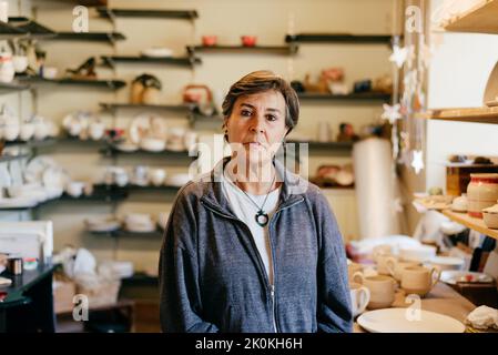 Serious middle aged female artisan looking at camera while resting after work in creative pottery studio Stock Photo