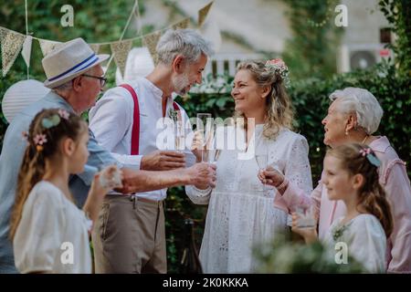 Mature bride and groom toasting with family at wedding reception outside in the backyard. Stock Photo
