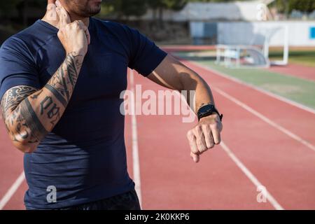 Crop unrecognizable male runner checking pulse on neck and watching at wristwatch during workout at stadium on sunny day Stock Photo