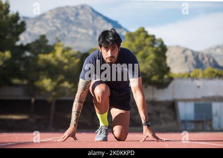 Front view of Hispanic male professional runner standing in crouch start position while getting ready for race at stadium Stock Photo