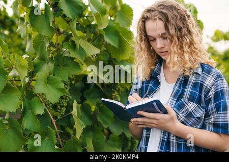 Curly-haired caucasian woman specialist writing on paper note book data about agriculture problems. Concept for smart farming, smart farmer, and smart Stock Photo