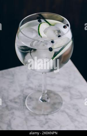 Glass of refreshing alcohol gin tonic cocktail with sliced cucumber and ice cubes on table Stock Photo