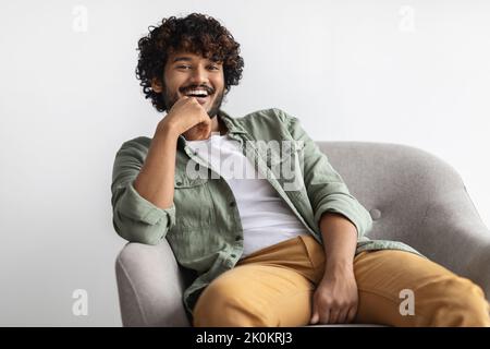 Cheerful indian guy sitting at arm chair at home Stock Photo