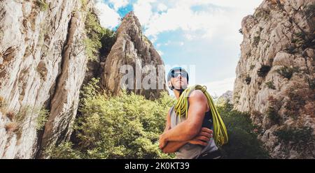 Portrait of smiling climber man in protective helmet and sunglasses with climbing rope on the shoulder standing in Paklenica park between rock cliff w Stock Photo