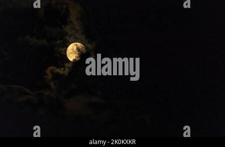 Full moon peaks around clouds on dark night Stock Photo