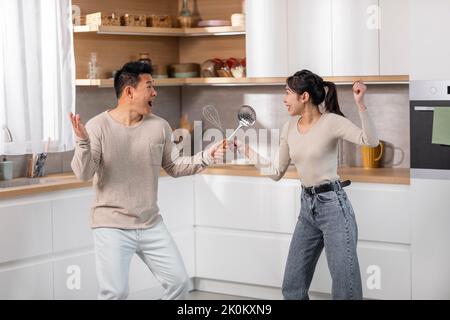 Positive chinese couple having fun while cooking at kitchen Stock Photo