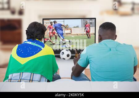 Two diverse friends sitting on the couch and watching football match Stock Photo