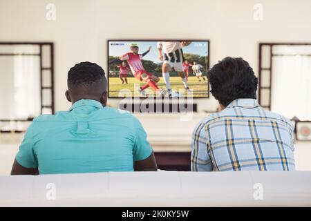 Two diverse friends sitting on the couch and watching football match Stock Photo