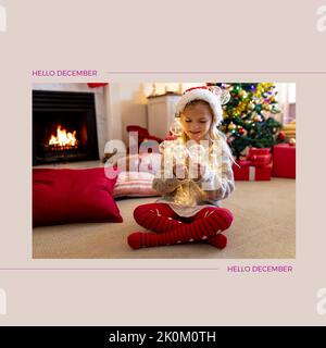 Composition of hello december text over caucasian girl at christmas Stock Photo