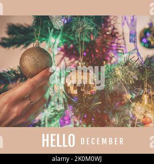 Composition of hello december text over christmas baubles and hand Stock Photo
