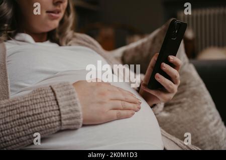 Pregnant woman siting on her sofa using her cellphone Stock Photo