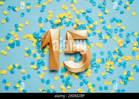 Number 15 fifteen golden celebration birthday candle on yellow and blue confetti Background. fifteen years birthday. concept of celebrating birthday, anniversary, important date, holiday Stock Photo