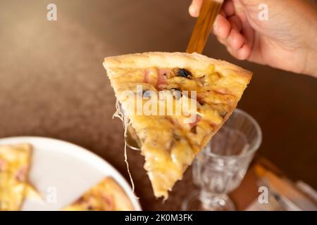 Slice of pizza with ham, mushrooms and cheese on a serving spatula and a man's hand. Closeup, sunflare Stock Photo