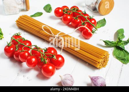 Spaghetti, basil and tomatoes isolated on a white wooden table. Stock Photo