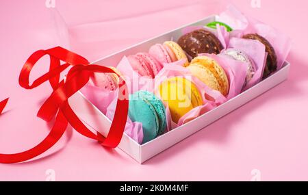 Colorful sweet macarons or macaroons, flavored cookies are in the paper box on the pink background. Stock Photo