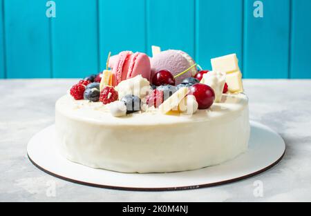 Tender white cake decorated with melted white chocolate, macaroons, meringues, berries and candies on concrete background. Stock Photo