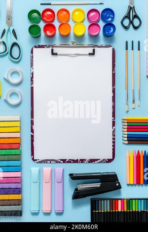 Colorful school supplies placed on blue background with white plain paper in the middle Stock Photo
