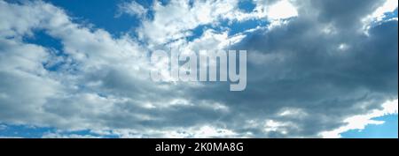 Blue sky with thunderclouds. The sun breaks through the clouds. Black clouds. Banner. Stock Photo