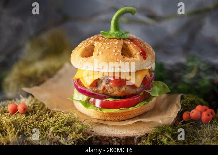 Halloween burger in a shape of pumpkin head jack lantern in a mystery forest. Scary cheeseburger on halloween party. Stock Photo