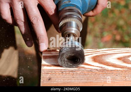 Wire brush for wood working, on a drill. Male hand is holding brushing machine electrical rotating with metal disk sanding a piece of wood. Stock Photo