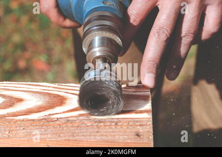 Wire brush for wood working, on a drill. Male hand is holding brushing machine electrical rotating with metal disk sanding a piece of wood. Stock Photo