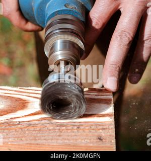 Wire brush for wood working, on a drill. Male hand is holding brushing machine electrical rotating with metal disk sanding a piece of wood. Stock Photo