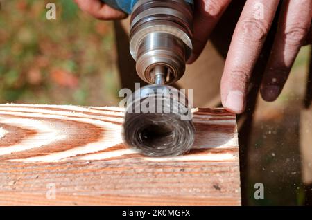 Wire brush for wood working, on a drill. Male hand is holding brushing machine electrical rotating with metal disk sanding a piece of wood. Stock Photo