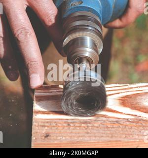 Wire brush for wood working, on a drill. Male hand is holding brushing machine electrical rotating with metal disk sanding a piece of wood. Stock Photo