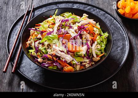 Chinese Chicken Salad with shredded chicken meat, mandarin oranges, crunchy noodles, red cabbage, napa cabbage, carrots, green onions in bowl Stock Photo