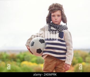 The weather wont let me play. a little boy standing outside in rainy weather with his soccer ball. Stock Photo