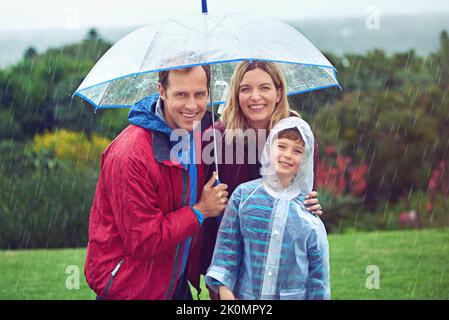 Rain or shine, we love the outdoors. Cropped portrait of a family of three standing outside in the rain. Stock Photo