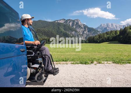 Caucasian young man using a hydraulic wheelchair car lift to get out of the van and enjoy a beautiful mountain landscape Stock Photo