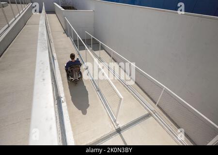 Man in a wheelchair use an accessible ramp. Stock Photo