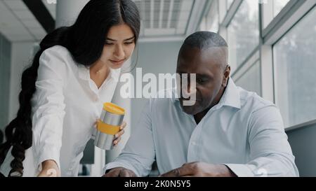 Two colleagues business partners office co-workers analyze paperwork check information. Arabian woman check documentation papers report help african Stock Photo
