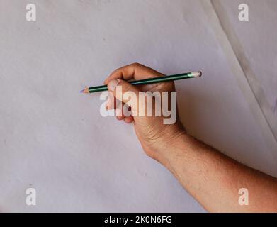 Male hand is holding a pencil on white background, starting to draw. Close up and copy space Stock Photo