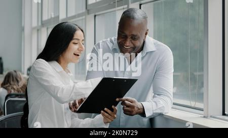 Diverse african and arabian colleagues multiracial people business partners stand near window discussing paper graphics strategic plans reading Stock Photo