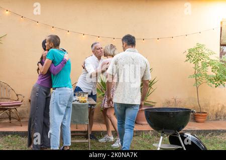 Multiethnic middle aged men and women friends greet each other and huddle together happily in barbecue in backyard. Stock Photo